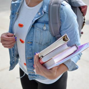 girl standing outside with a backpack and school books in her hands