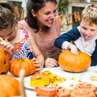 kids and their mom sit at a table outside and play with pumpkin carvings