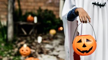 a kid in their halloween costume stands with his halloween pumpkin for trick or treating